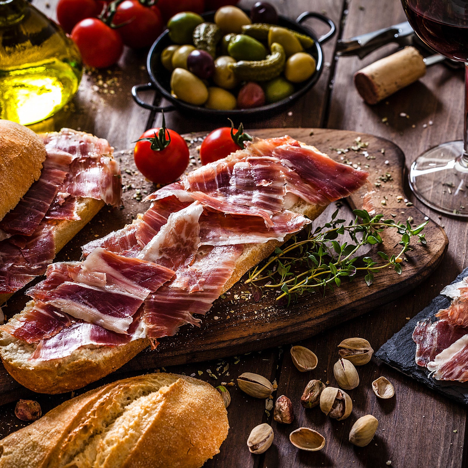 Spanisches Olivenöl und Tapas-Zutaten auf einem Holzbrett